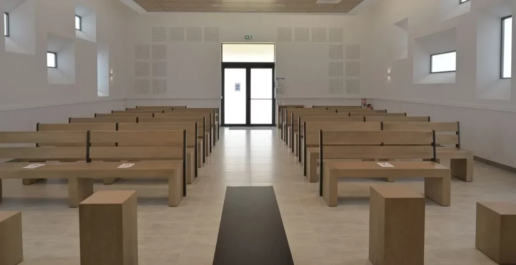 Grande salle de cérémonie funéraire lumineuse avec bancs en bois alignés et allée centrale