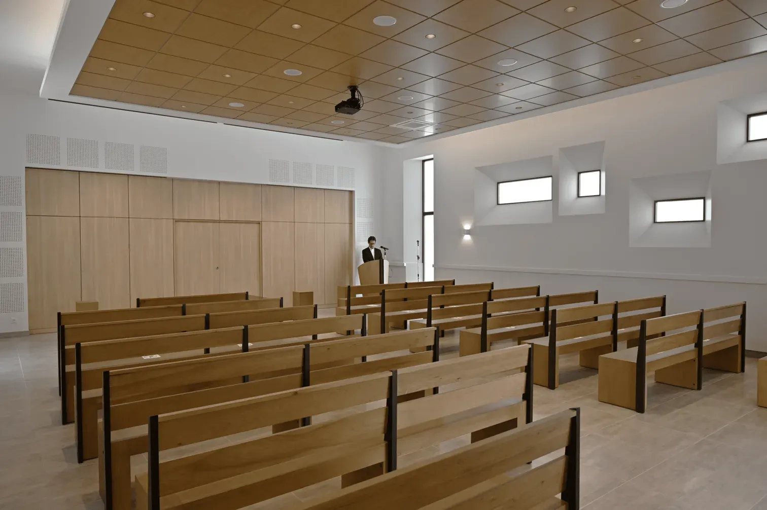 Grande salle de cérémonie funéraire lumineuse avec bancs en bois alignés et allée centrale